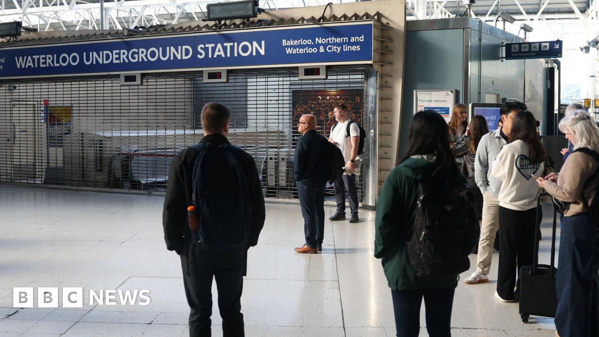 Commuters stand outside the closed entrance to Waterloo Underground Station, where shutters are pulled down.