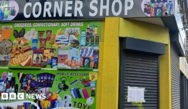 Image shows the brightly coloured exterior of The Corner Shop in Picton Road, Liverpool. Advertisements for vapes, stationery, toys and sweets adorn one of its walls. The shutters are down and there is an enforcement notice taped to them.