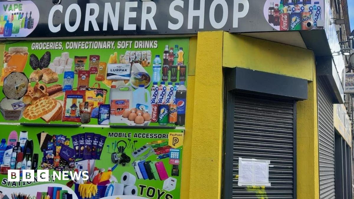 Image shows the brightly coloured exterior of The Corner Shop in Picton Road, Liverpool. Advertisements for vapes, stationery, toys and sweets adorn one of its walls. The shutters are down and there is an enforcement notice taped to them.