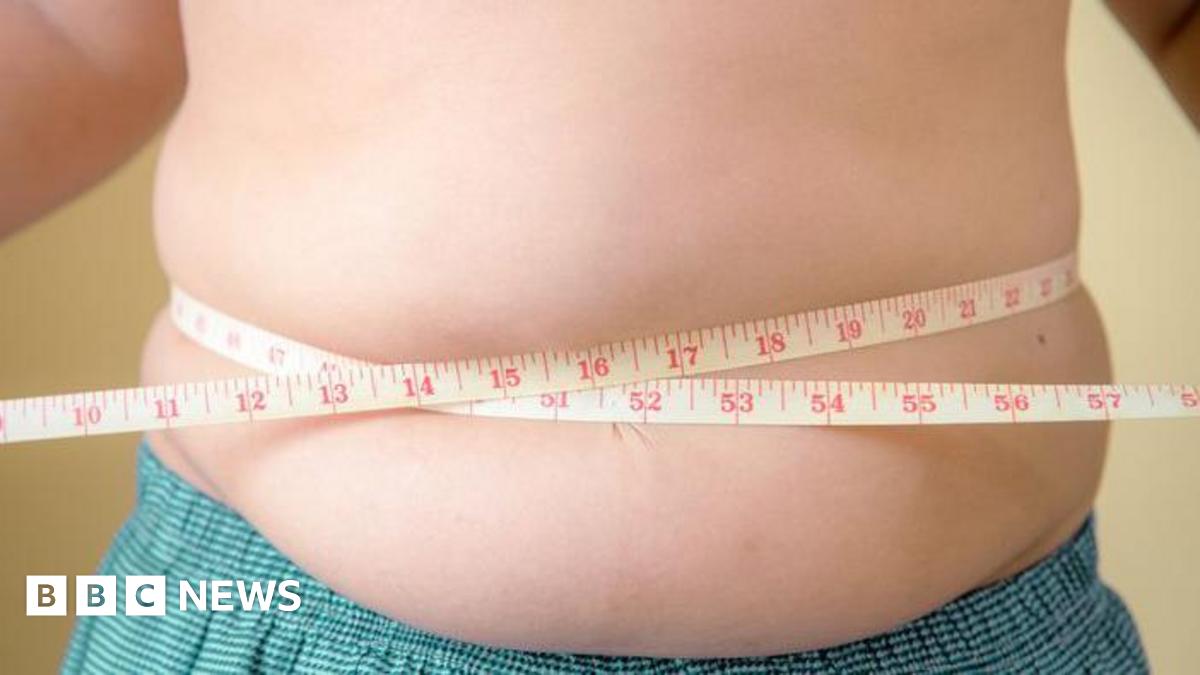 An overweight young boy holds a tape measure around his waist