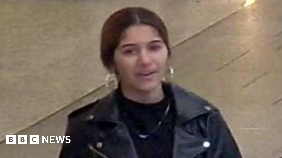 Pantica Sali wearing a black leather jacket over a black top with a chain around her neck. She has hooped earrings and black hair tied back.