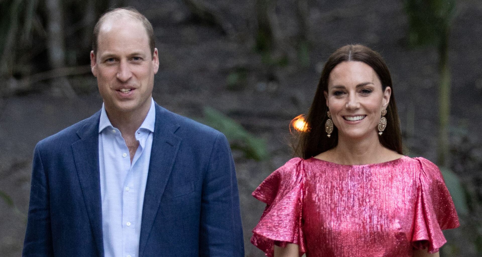 Prince William wears a navy suit with a light blue shirt and Kate Middleton wears a metallic pink dress