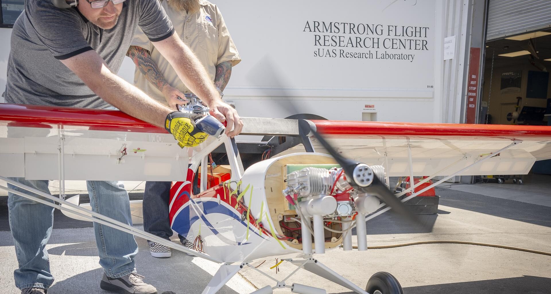 One man manages engine speed with a hand-held controller, while another firmly holds the subscale aircraft in place.