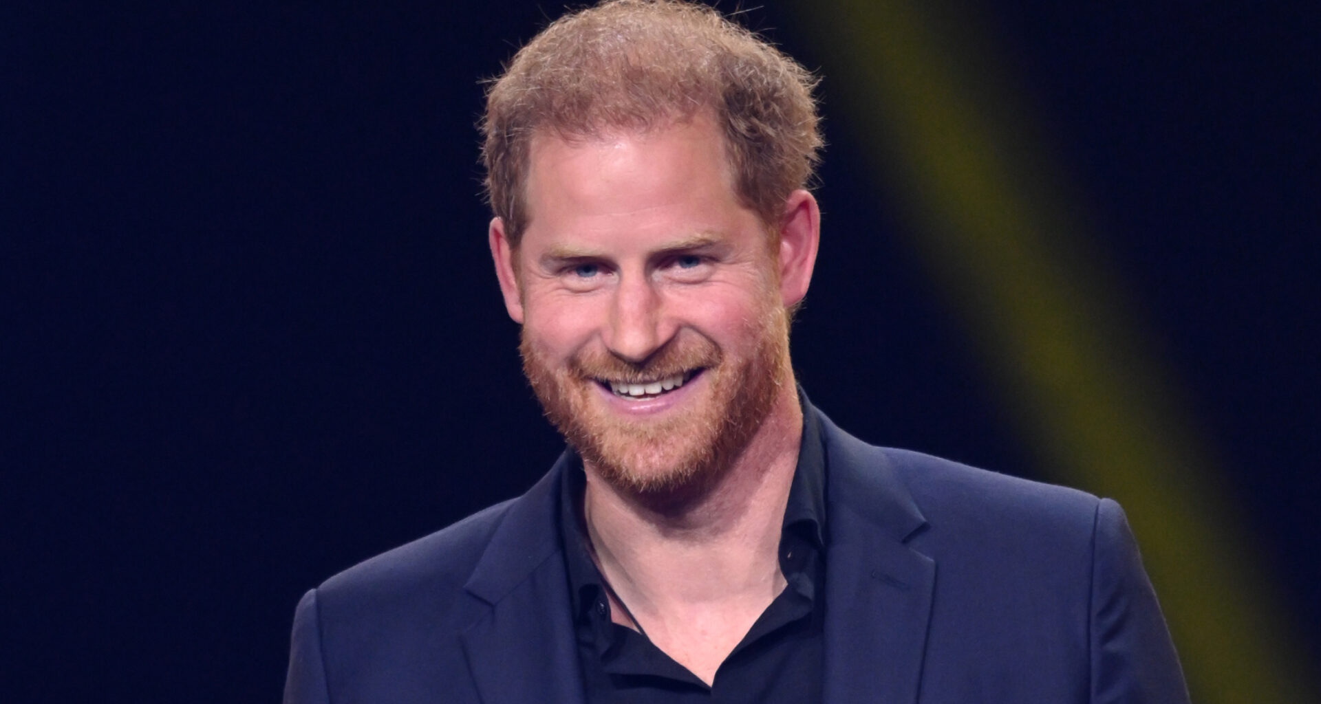 Prince Harry smiles while wearing a navy suit