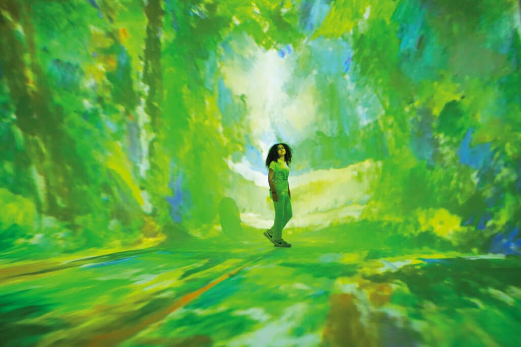 A young woman standing in an immersive gallery at the FRAMELESS exhibition