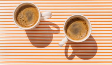 Two white coffee cup on orange striped table at direct sunlight. Top view with shadow.