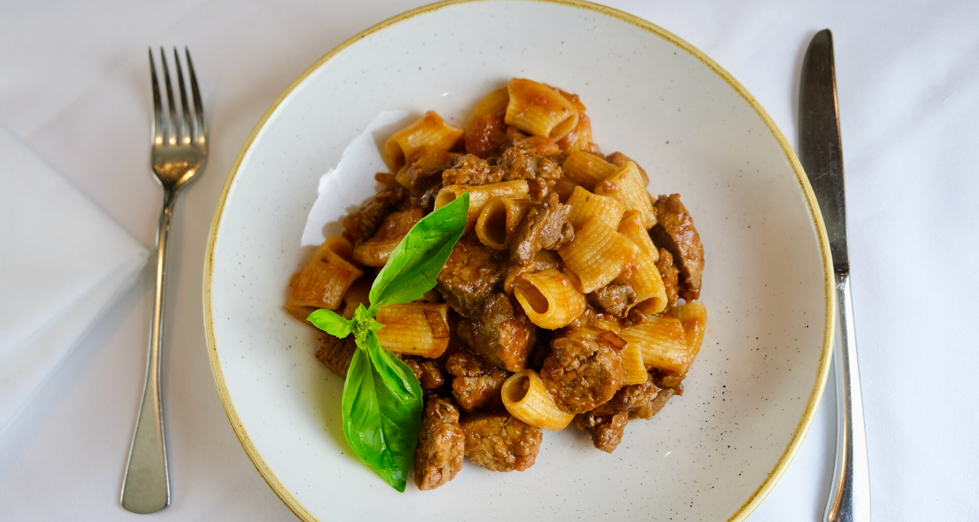 A plate of rigatoni pasta with meat sauce and a basil garnish.