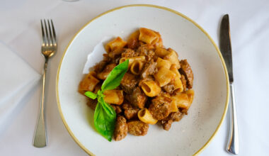 A plate of rigatoni pasta with meat sauce and a basil garnish.