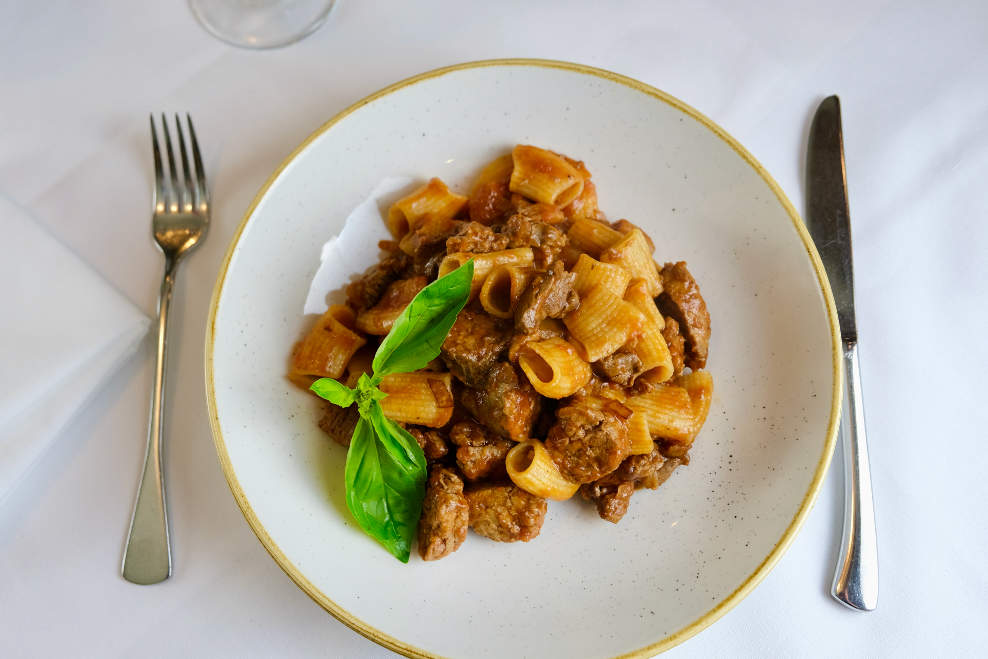 A plate of rigatoni pasta with meat sauce and a basil garnish.