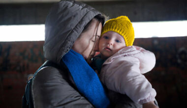 A women with her eyes closed holding a child in her arms.