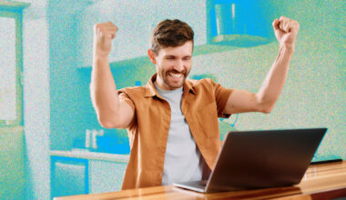 A young man looking excited while sitting at a table using a laptop.