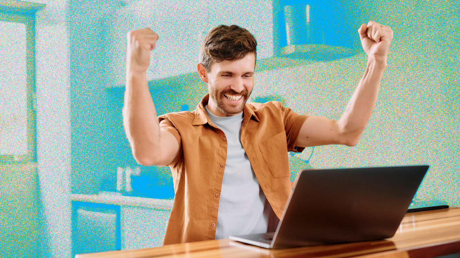 A young man looking excited while sitting at a table using a laptop.