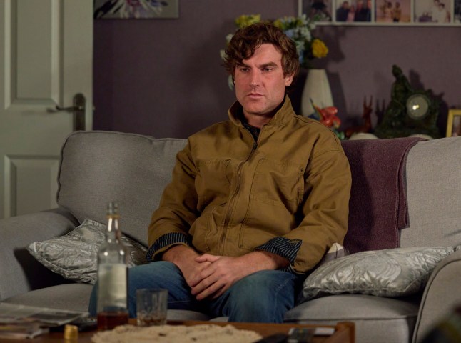 Theo Silverton looking into the middle distance with a bottle of alcohol near him in Coronation Street.