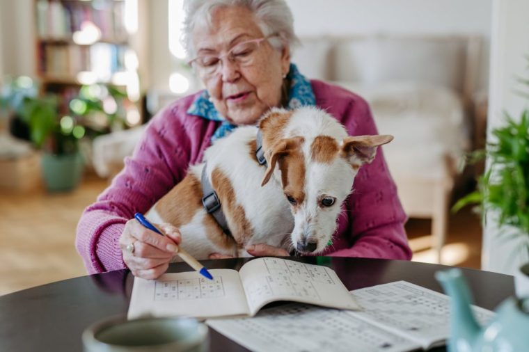 A woman completes a Sudoku puzzle while cuddling her dog