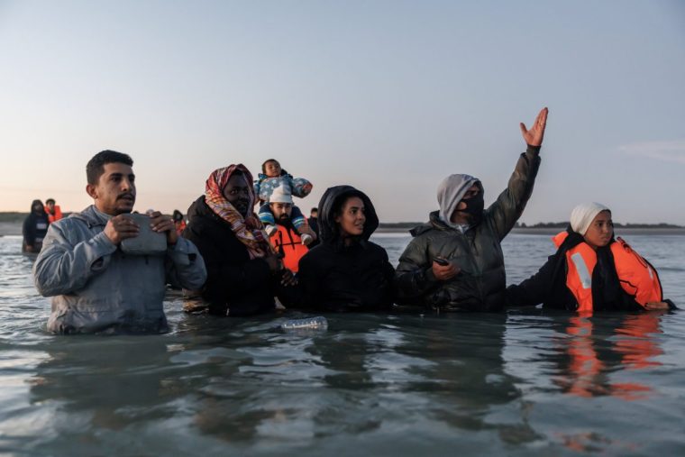 GRAVELINES, FRANCE - SEPTEMBER 19: Traffickers hold people back as migrants wade into the water to get to a 'taxi boat' to take them across the channel to the UK at dawn on September 19, 2025 in Gravelines, France. Removals of small boat migrants under the UK's landmark migration treaty with France have begun after the historic agreement came into force in recent weeks. (Photo by Dan Kitwood/Getty Images)