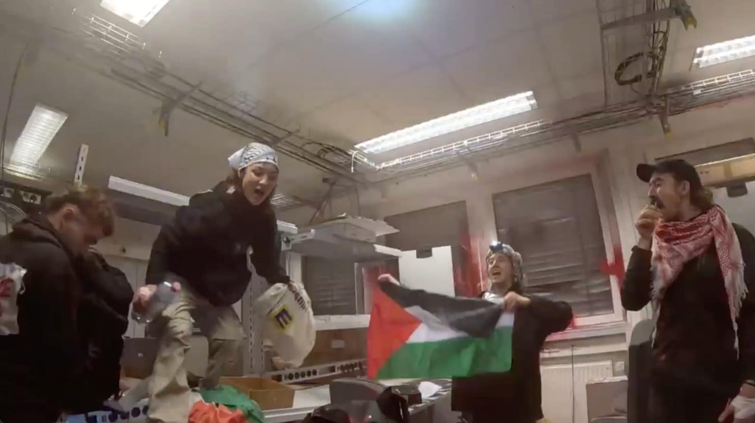 Palestine Action activists inside Elbit's Ulm factory holding a Palestine flag, climbing on and damaging equipment. 