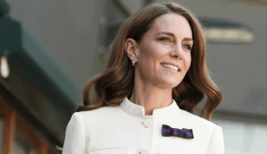 Kate Middleton wearing a white blazer with a purple bow pin and smiling
