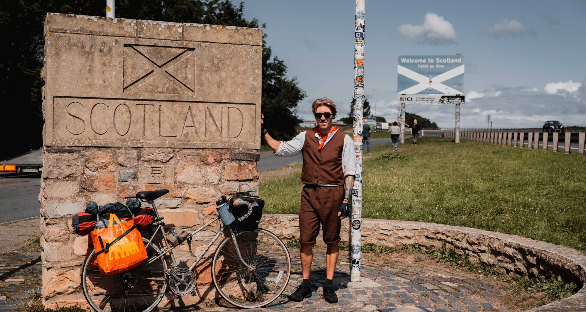 A man stands next to a sign for Scotland with his bike