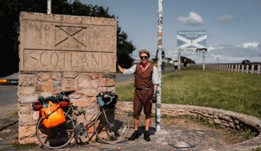 A man stands next to a sign for Scotland with his bike