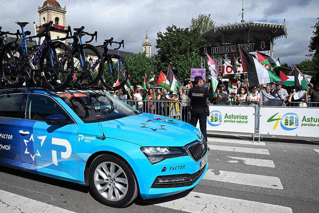 Pro-Palestinian protesters wave flags as Team Israel Premier Tech's team car drives past in Vegadeo at the start of the 15th stage of the Vuelta a Espana cycling tour, a 167 km race between A Veiga/Vegadeo and Monforte de Lemos, on September 7, 2025. (Photo by Miguel RIOPA / AFP)