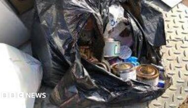 An open black bin liner with rubbish spilling out into the street including cans