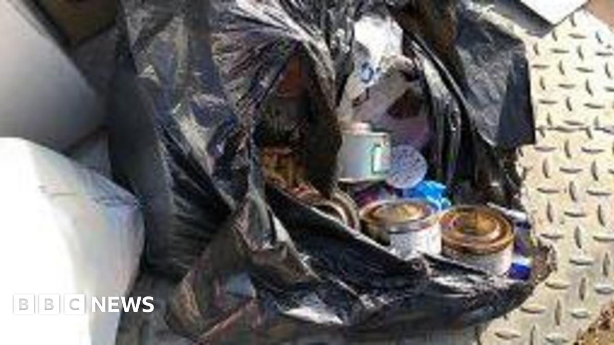An open black bin liner with rubbish spilling out into the street including cans