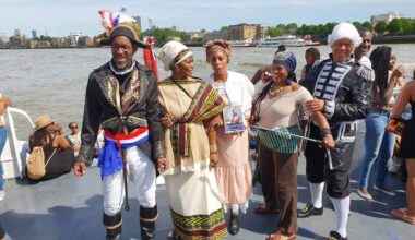 an actor onstage, portraying a Black woman in Barbados, interacts with a radio