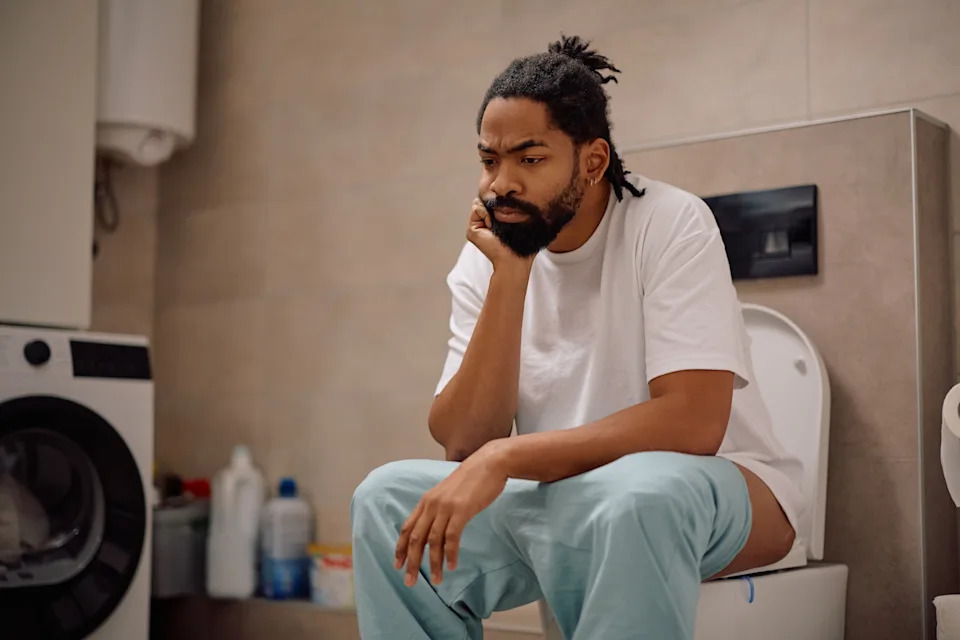 Pensive African American man sitting on a toilet in the morning.