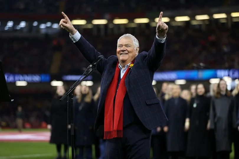 Max Boyce in front of a mic with his hands raised