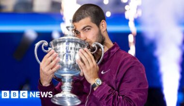 Carlos Alcaraz, wearing a purple Nike jacket, kissing the US Open trophy.