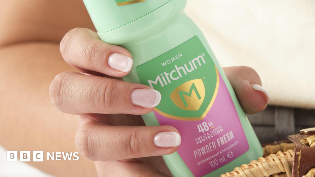 A hand holding a green and pink bottle of Mitchum powder-fresh roll-on deodorant.