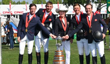 A show jumping team on a podium with a large trophy.
