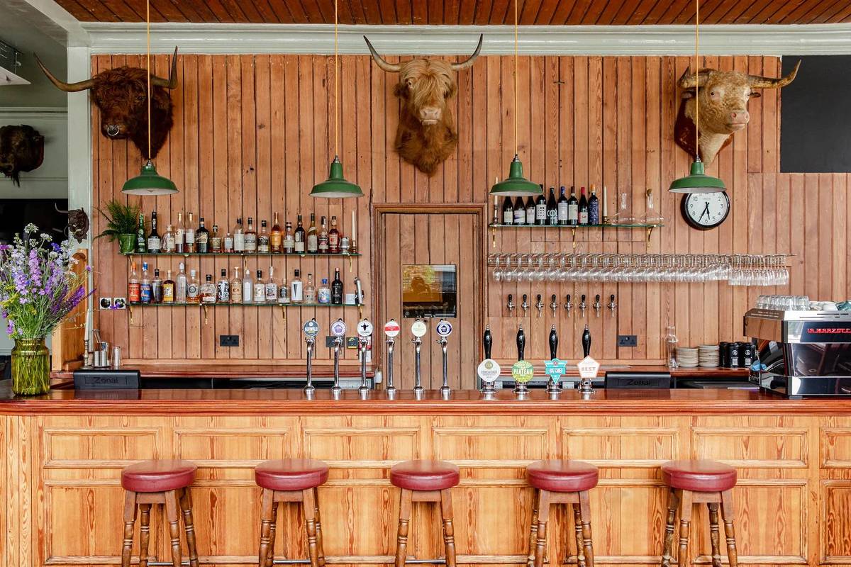 the wood panelled bar at the bull and last pub, with beer taps, bottles of liquor, and mounted taxidermied animal heads