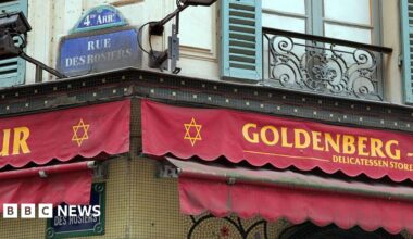 Red scalloped awning advertises Goldenberg's delicatessen stre in yellow font, with the Jewish star of David printed next to the restaurant sign. Above the sign is the street name Rue des Rosiers, 4th arrondisement, in white writing on blue tiling.