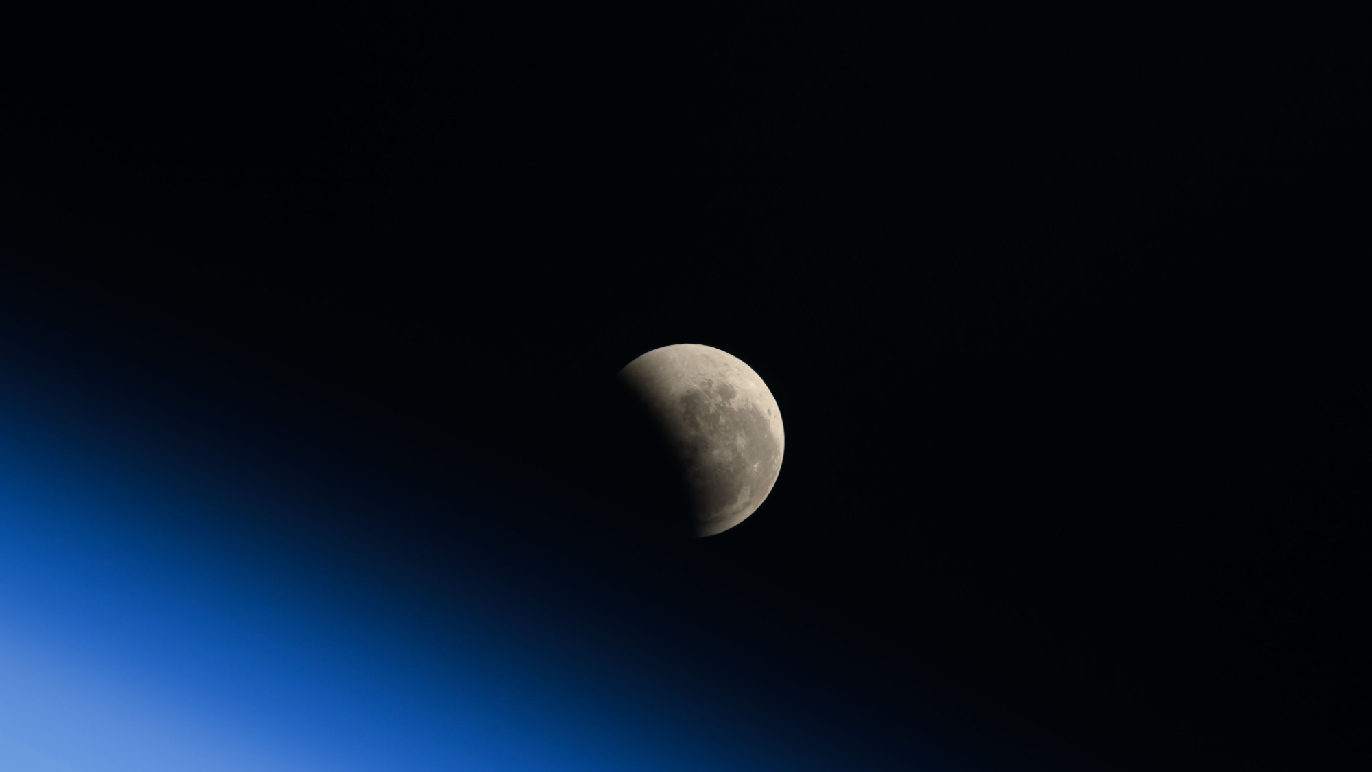 image of a lunar eclipse seen from the international space station, showing part of the gray moon hidden in shadow