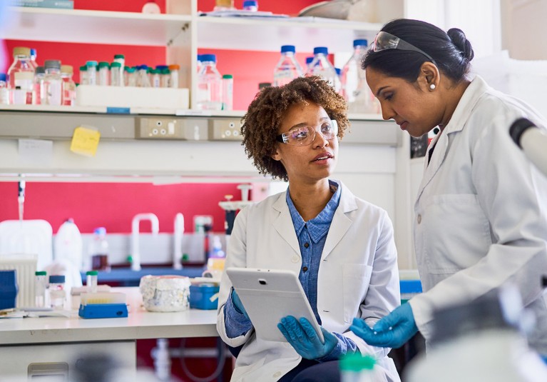 Two female scientists going over data on a digital tablet while working together in a lab.