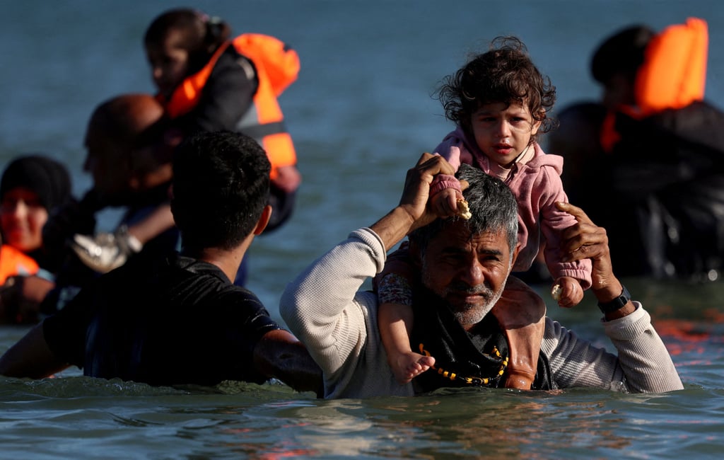Migrants wade through the sea to board an inflatable dinghy leaving the coast of northern France to cross the English Channel on August 25. Photo: Reuters