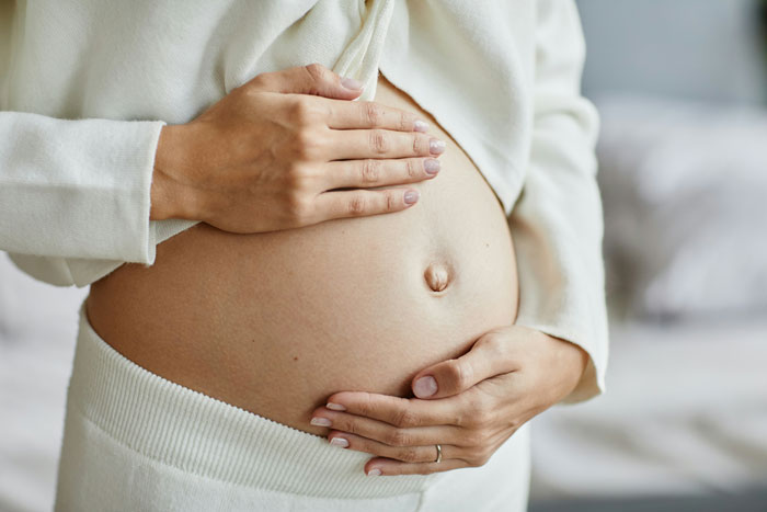 Close-up of hands gently holding a pregnant belly, illustrating a doctor’s surprising discovery of hair and teeth inside.