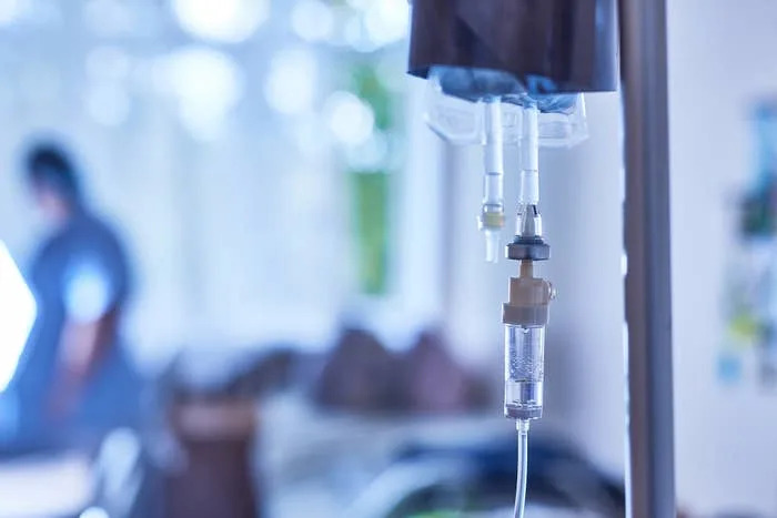 IV drip in a hospital room with a blurred healthcare worker in the background, symbolizing medical care and health industry focus