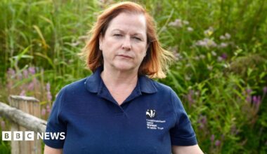 Natalie Buttriss is wearing a navy polo top and is standing in front of a bank of high reeds, staring straight at the camera.
