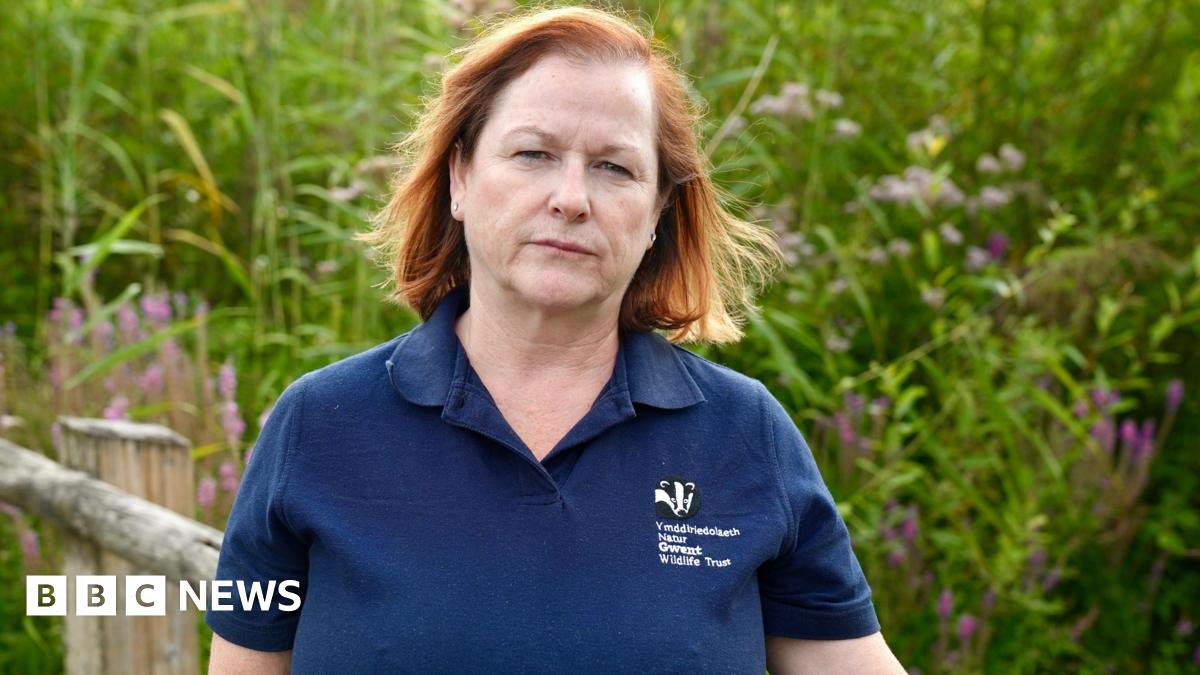 Natalie Buttriss is wearing a navy polo top and is standing in front of a bank of high reeds, staring straight at the camera.