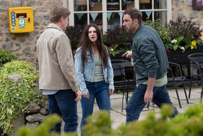 Injured Victoria stands between Robert and John in Emmerdale