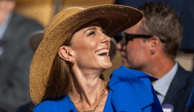 Kate Middleton wearing a blue dress and a straw hat looking up and laughing