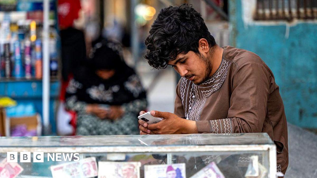 A man sitting at a money exchange stall playing on his phone.