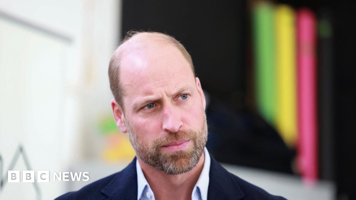Prince William looks to the right of the camera, he is wearing a light blue shirt with a navy blazer.