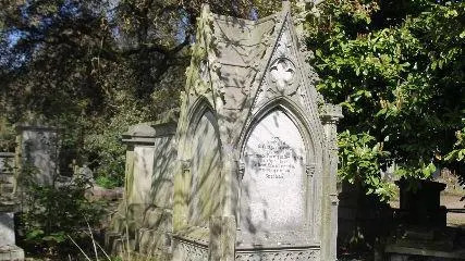 A grey stone monument with a roof housing the remains of Emily Fazakerley and her family. The inscription reads "Sacred to the memory of Emily Augusta Fazakerley third daughter of Henry Hawarden Fazakerley and Harriet his wife. Who departed this life an Banwell Abbey in Somersetshire on 17th day of June 1888. 'Thy will be done'."