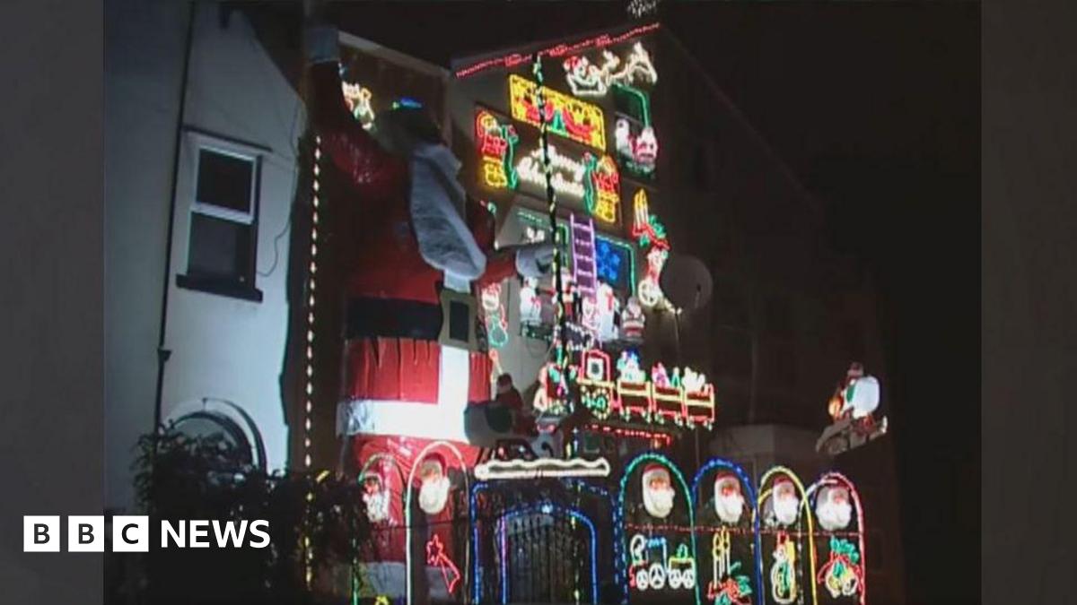 A three storey house decorated in Christmas lights with a giant Father Christmas
