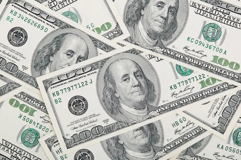 A pile of scattered U.S. hundred-dollar bills featuring Benjamin Franklin's portrait, symbolizing wealth and finance
