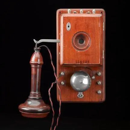 A mahogany box mounted on the wall, about the size of a house brick. It has a round silver bell with three buttons. On the left there is a hook, where the earpiece hangs. A cable connects it to the main body 