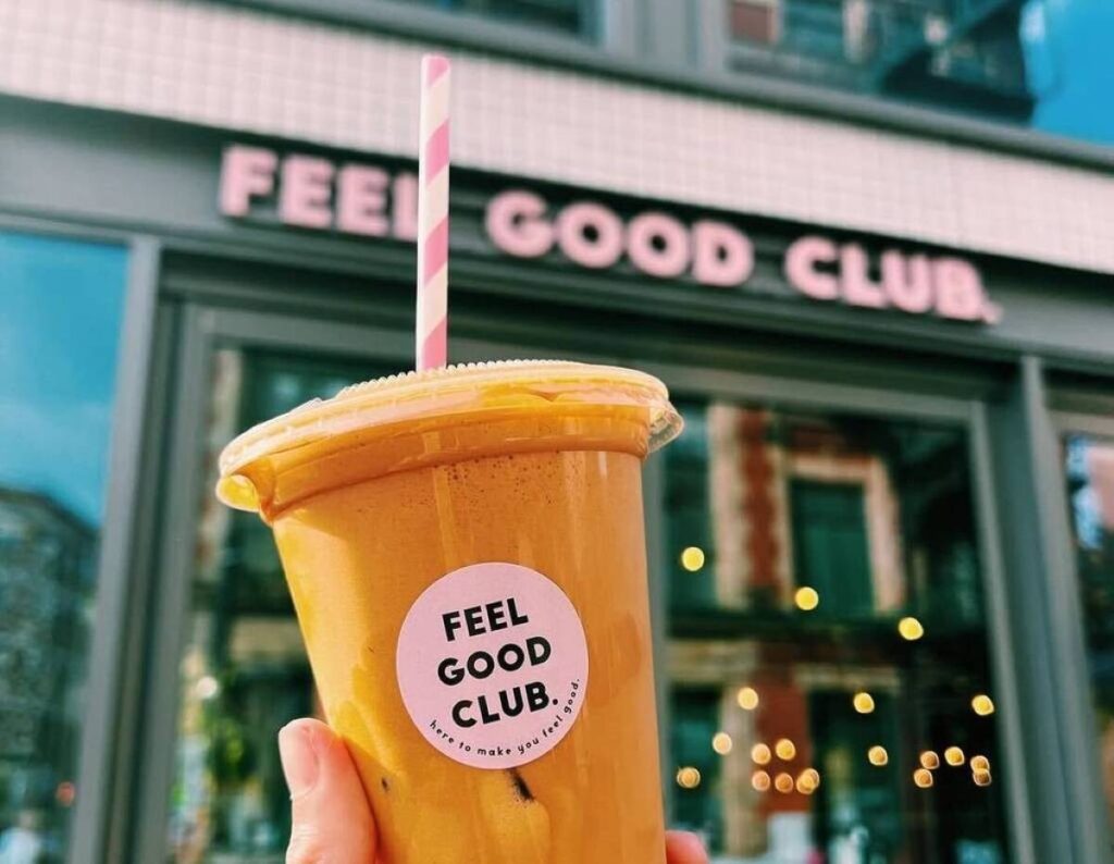 feel good club iced coffee held up in front of shop in manchester